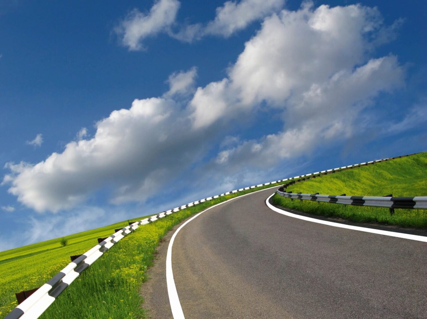 A winding road in a green field with clouds in the sky.