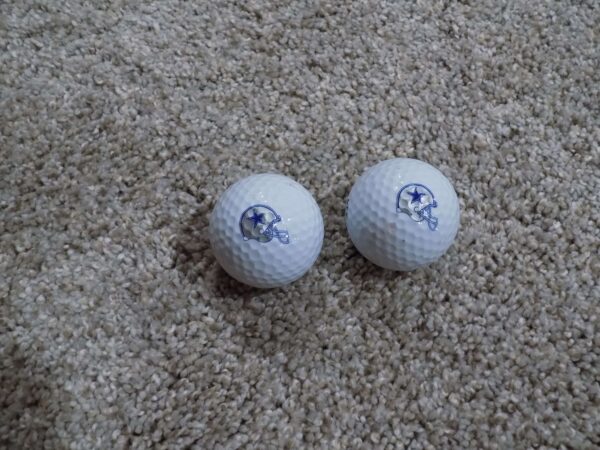 Two Dallas Cowboys golf balls on carpet.