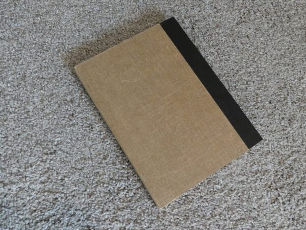 Tan book with black spine on carpet.